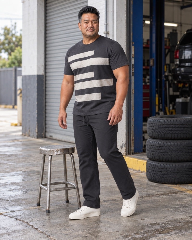 Charcoal Oat Wide Track outfit worn at an ordinary neighborhood auto-service courtyard with a roll-up door, painted curb, metal stool and stacked plain tires