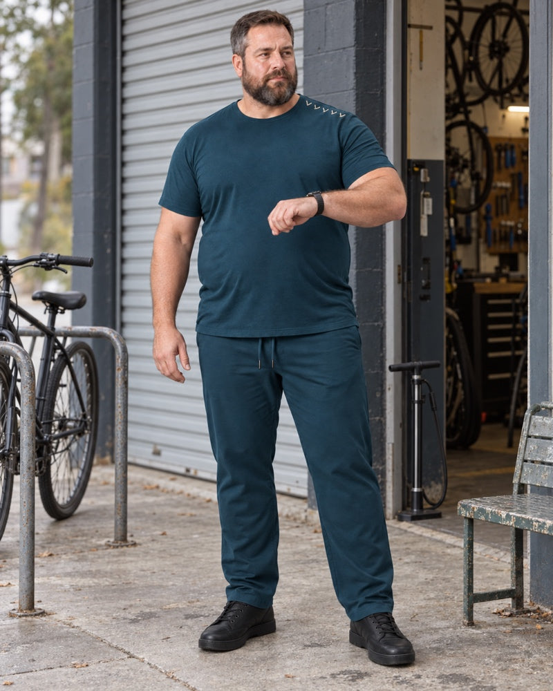 Deep Teal Oat Northline Ticks outfit worn at an ordinary neighborhood bicycle-repair entrance with a roll-up door, floor pump, metal bench and plain bike rack