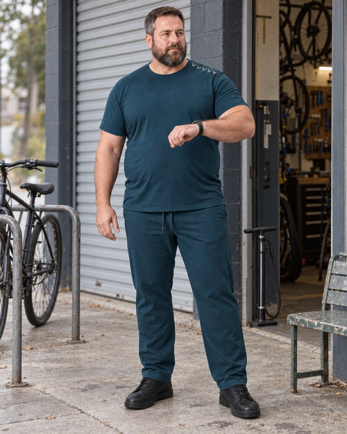 Deep Teal Oat Northline Ticks outfit worn at an ordinary neighborhood bicycle-repair entrance with a roll-up door, floor pump, metal bench and plain bike rack